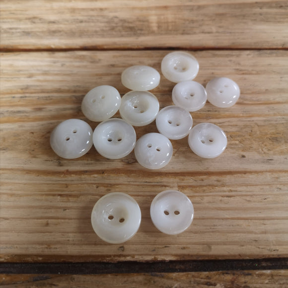 Group of shiny cream 2 hole buttons on a wooden surface.